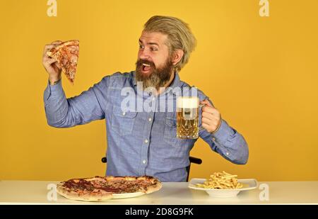 Frites. Gars au bar qui boit du verre de bière et qui mange de la pizza. Santé. regardant le football à la télévision. restauration rapide américaine. Bonne barbe avec bière et pizza. Cuisine italienne. Banque D'Images