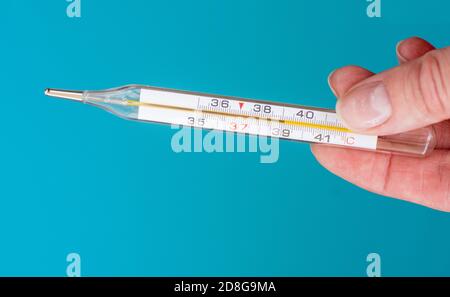 La main femelle en gros plan tient un thermomètre sur fond bleu. Le thermomètre indique une température corporelle élevée Banque D'Images