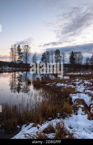 Vue sur le lac à la fin de l'automne au coucher du soleil avec de l'herbe sèche et la première neige en premier plan. Banque D'Images