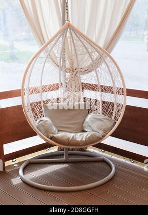 Chaise suspendue en rotin en osier nichée sur la terrasse d'une maison. Endroit confortable pour se reposer et se détendre. Intérieur moderne. Banque D'Images