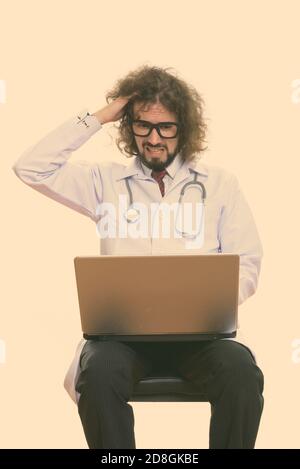 Studio shot of a souligné l'homme médecin à l'aide d'un ordinateur portable avec main sur sa tête Banque D'Images