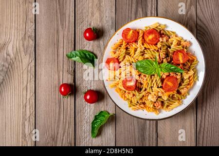 Fusilli - pâtes italiennes classiques de blé dur avec viande de poulet, tomates cerises, basilic dans une sauce tomate dans un bol blanc sur table en bois méditerranéenne Banque D'Images