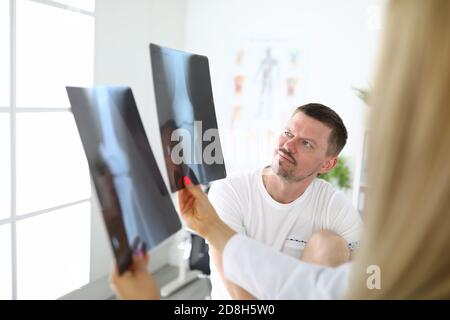 Un jeune patient atteint d'une jambe douloureuse regarde la radiographie de articulation du genou avec un médecin en clinique Banque D'Images