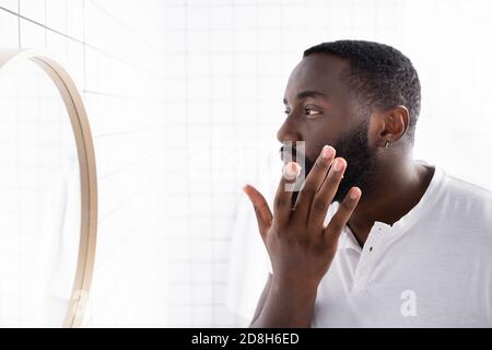 homme afro-américain appliquant un traitement pour renforcer la croissance de la barbe Banque D'Images