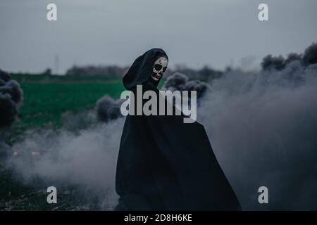 La jeune femme se tient sur le terrain en costume de Halloween de la mort sur fond de fumée noire. Concept Halloween. Maquillage de crâne de sucre. Banque D'Images