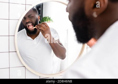 homme afro-américain vérifiant la gomme avec une brosse à dents en bambou Banque D'Images