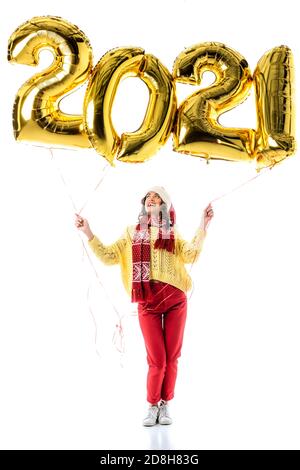 jeune femme joyeuse en chapeau de père noël et écharpe tenant des ballons avec des nombres isolés sur blanc Banque D'Images