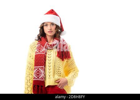 jeune femme brune en chapeau de père noël et foulard rouge debout avec main dans la poche isolée sur blanc Banque D'Images