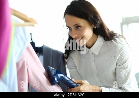 Femme souriante repassant sa chemise avec un défroisseur dans le linge Banque D'Images