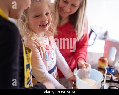 Une fille de 3 ans fait de la pâte à gâteau avec sa mère et sœur aînée à la maison Banque D'Images