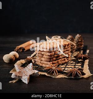 Spéculoos empilés avec du ruban d'emballage enveloppé sur une grille de refroidissement noire, décoré avec des étoiles en bois, des bâtons de cannelle et des étoiles anis, en arrière-plan f Banque D'Images