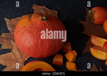 Citrouille entière et morceaux frais crus sur fond de pierre avec feuilles d'automne Banque D'Images