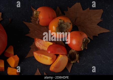 Kaki entier et tranché avec des feuilles d'automne brunes sur un pierre Banque D'Images