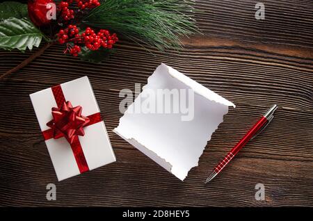 Un cadeau pour la nouvelle année et une carte postale vide pour le texte. Composition du nouvel an sur fond de bois. Une feuille de cadeaux en papier et un stylo Banque D'Images