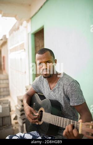 Un homme adulte joue une guitare à l'extérieur de sa maison sur l'île de Maio, à Cabo Verde. Banque D'Images
