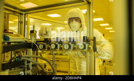 Dans l'usine de fabrication, photo d'un scientifique travaillant sur des vêtements de protection stériles sur des machines d'impression 3D industrielles. Fabrication biotechnologique Banque D'Images