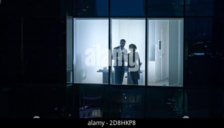 Prise de vue aérienne depuis l'extérieur du Skyscraper : homme d'affaires et femme d'affaires parlant en se tenant debout dans la fenêtre du bureau. Photo du quartier des affaires Banque D'Images