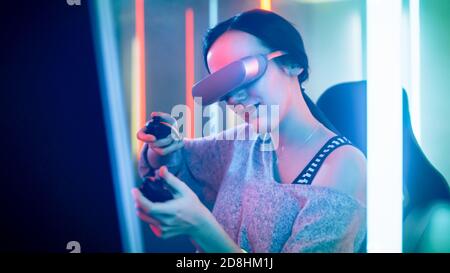 Pro Gamer Girl Wearing Virtual Reality Headset joue le tournage de jeu vidéo en ligne avec des manettes de commande. Couleurs fluo rétro dans la chambre. Banque D'Images