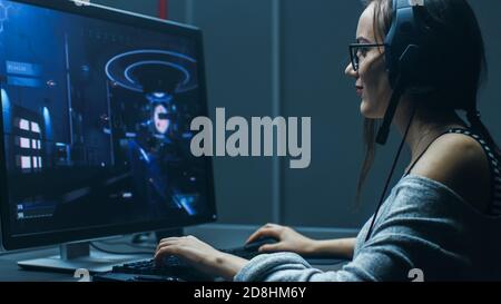 Photo de la belle professionnelle de joueur fille jouant dans jeu vidéo en ligne de jeu de tir de première personne sur son ordinateur personnel. Décontracté mignon Geek porter Banque D'Images