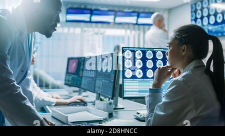 Deux scientifiques du laboratoire de recherche sur le cerveau travaillent. Les neurologues utilisent un ordinateur personnel avec l'IRM, les scannages CT montrent des images du cerveau. Banque D'Images