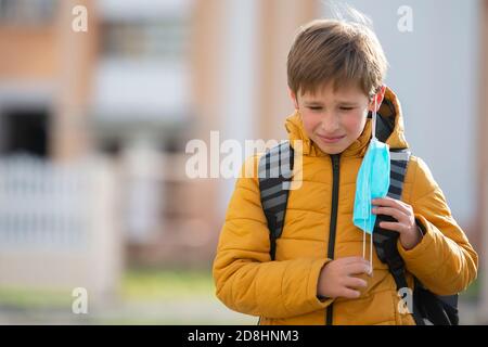 Un enfant triste prend son masque médical pour le coronavirus après l'école. Banque D'Images