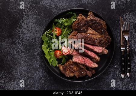 Steak de bœuf grillé aux épices sur une assiette noire, vue du dessus. Banque D'Images