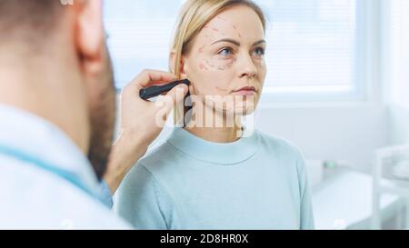 Prise de vue au-dessus de l'épaule d'une patiente assise patiemment tandis que le chirurgien plasticien dessine des lignes sur son visage pour l'opération de Facelift. Banque D'Images