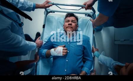 Top Down Shot, paramédics, médecins et infirmières déplaçant un homme gravement blessé sur un brancard. Le personnel médical pousse Gurney avec la victime de l'accident vers Banque D'Images