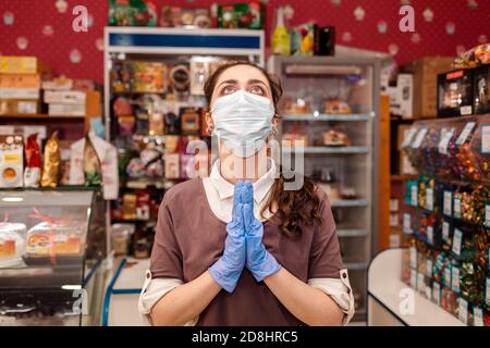 Les petites entreprises pendant la pandémie. Une travailleuse dans un masque médical et des gants en caoutchouc, la répand les mains et regarde avec espoir. Concept de protec Banque D'Images