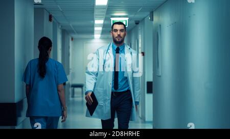 Un beau médecin portant un manteau blanc avec stéthoscope se promène dans le couloir de l'hôpital. Clinique moderne et lumineuse avec un personnel professionnel. Banque D'Images