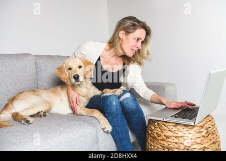 Une belle femme avec son chien Golden Retriever utilisant un ordinateur portable sur le canapé Banque D'Images