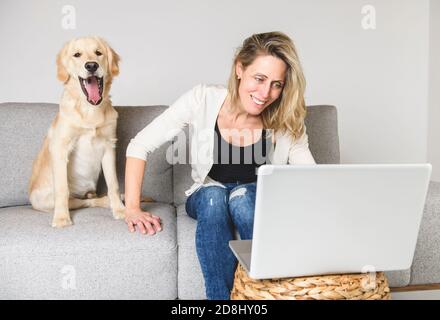 Une belle femme avec son chien Golden Retriever utilisant un ordinateur portable sur le canapé Banque D'Images