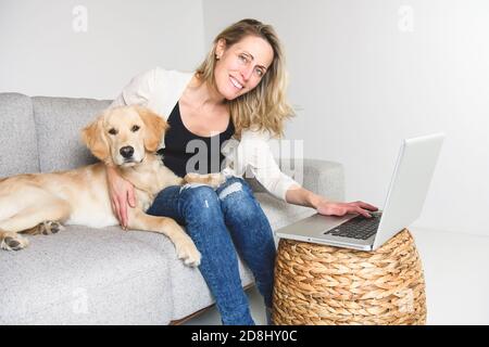 Une belle femme avec son chien Golden Retriever utilisant un ordinateur portable sur le canapé Banque D'Images