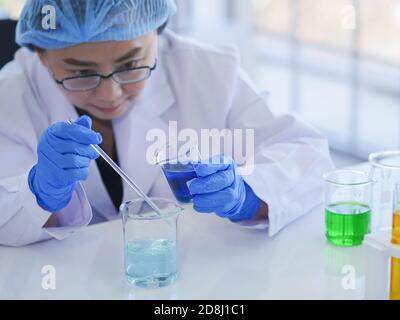Femmes scientifiques senior travaillant seules dans le laboratoire se préparer à mélanger les deux liquides dans un bécher pour un biologique expérience en sciences chimiques à réaliser Banque D'Images