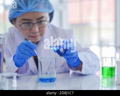 Une scientifique senior utilise sa concentration pour travailler dans le laboratoire. Mélanger deux types de liquides pour les expériences de chimie biologique Banque D'Images