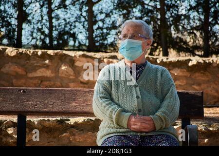 Femme plus âgée assise sur un banc de parc avec son masque activé Banque D'Images