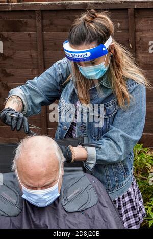 Un coiffeur mobile indépendant s'occupe de l'un des cheveux de son client dans le jardin arrière pendant la pandémie de Covid 19 ou de Covid 19 en Angleterre. Banque D'Images