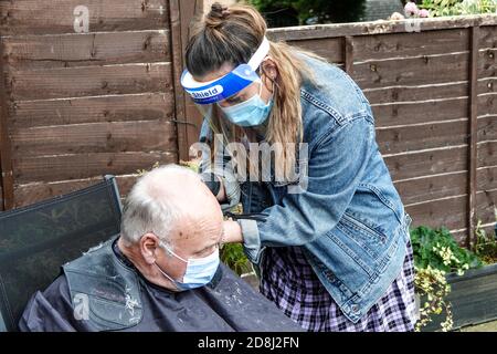 Un coiffeur mobile indépendant s'occupe de l'un des cheveux de son client dans le jardin arrière pendant la pandémie de Covid 19 ou de Covid 19 en Angleterre. Banque D'Images