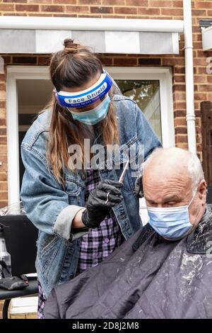 Un coiffeur mobile indépendant s'occupe de l'un des cheveux de son client dans le jardin arrière pendant la pandémie de Covid 19 ou de Covid 19 en Angleterre. Banque D'Images