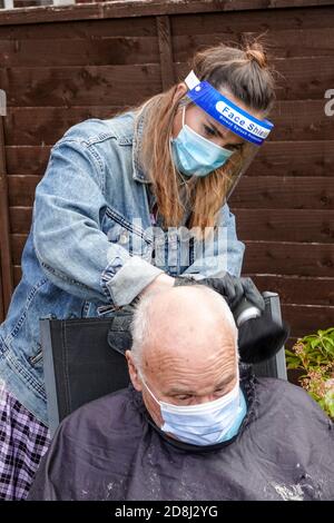 Un coiffeur mobile indépendant s'occupe de l'un des cheveux de son client dans le jardin arrière pendant la pandémie de Covid 19 ou de Covid 19 en Angleterre. Banque D'Images