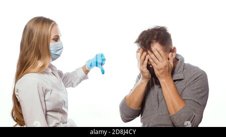 Une jeune infirmière en uniforme blanc montre le pouce jusqu'à un homme ou un patient d'âge moyen triste. Concept de test Covid Banque D'Images