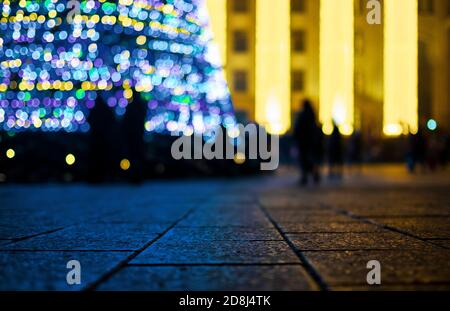 Sapin de Noël aux lumières luminescentes, effet de flou. Pavés en gros plan au premier plan. Banque D'Images