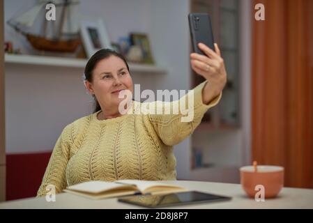 Femme âgée en chandail jaune emportant un selfie avec un smartphone Banque D'Images