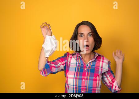 Jolie jeune femme portant un masque de protection à bouche ouverte. Découper sur fond jaune. Concept de quarantaine Banque D'Images