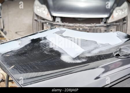 Réparation de la carrosserie, application PuTTY gros plan. Le mécanicien répare la voiture. Travailler après l'accident en travaillant le primaire de ponçage avant de peindre. Banque D'Images
