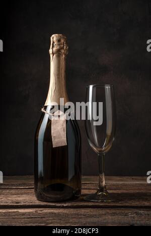 Une bouteille de champagne fermée et un verre de vin vide sur fond de bois. Banque D'Images