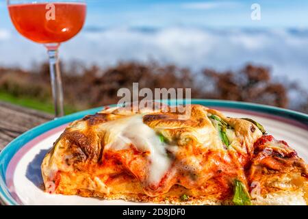 Gros plan macro de pizza tranche sur plaque sur balcon terrasse Autour de la rose rouge boisson de vin dans le jardin à l'extérieur dans le bleu Montagnes de Ridge avec brouillard brouillard brumeux au-dessus de vi Banque D'Images