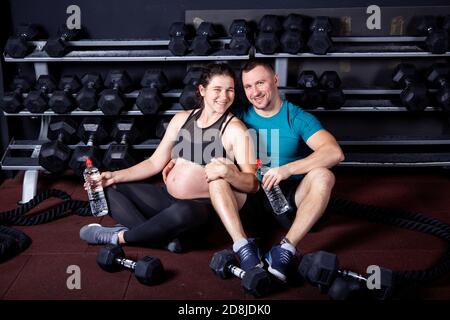 Une femme enceinte va faire du sport avec son mari en salle de sport pour un entraînement multidisciplinaire. Couple athlètes s'attendant à bébé tout en se reposant après l'entraînement et les exercices Banque D'Images