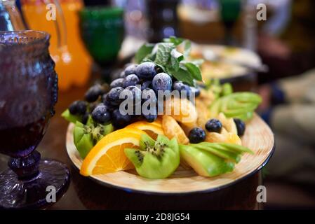 Plat de fruits dans un restaurant : bouquet de raisins noirs saupoudrés de sucre en poudre, kiwi haché au figuré, tranches d'orange et de mandarine, pommes Banque D'Images