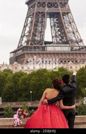 Bientôt marié, un jeune couple pose devant l'emblématique tour Eiffel pour son album photo de mariage. La mariée et le marié sont formellement habillés Banque D'Images